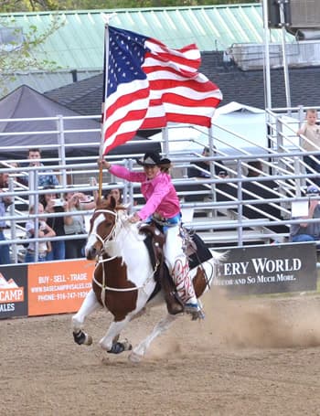 Rider in a pink shirt carrying the American flag at a gallop during the grand entry