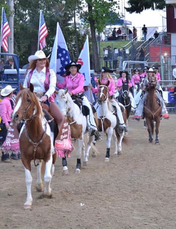 Rodeo queens and riders on horseback with American flags in the Patriot's Day grand entry
